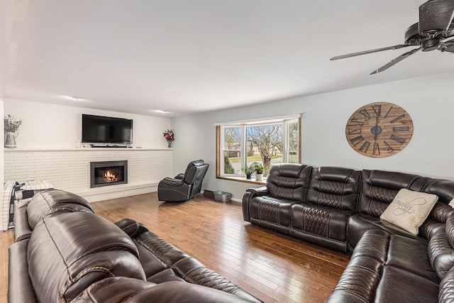 living room with hardwood / wood-style floors, a brick fireplace, a ceiling fan, and baseboards