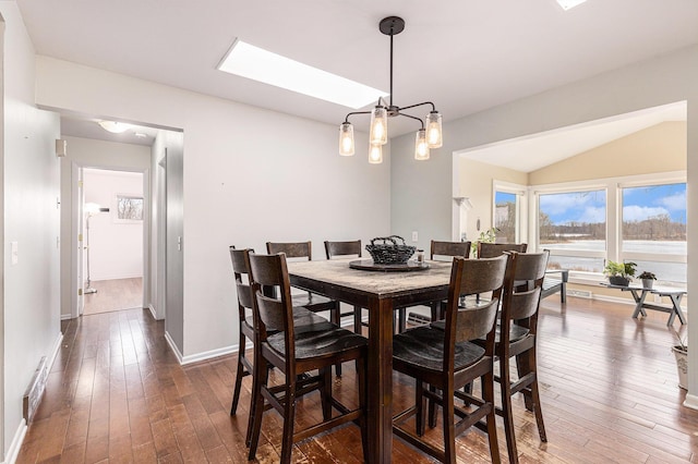 dining space featuring a chandelier, vaulted ceiling with skylight, dark wood-style flooring, and baseboards