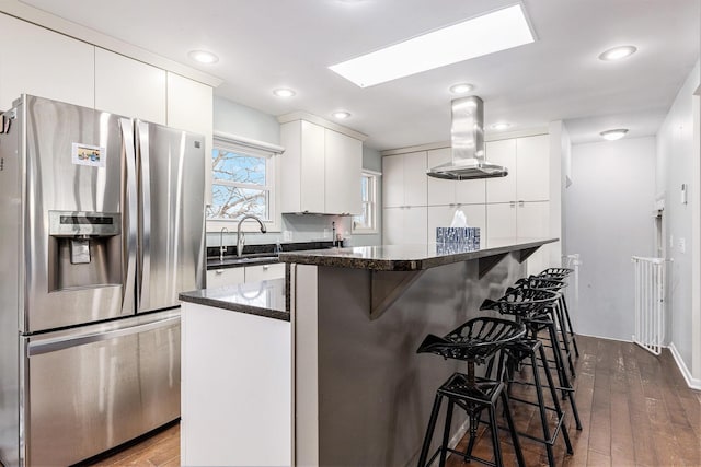 kitchen with island exhaust hood, stainless steel refrigerator with ice dispenser, a breakfast bar area, white cabinetry, and a sink