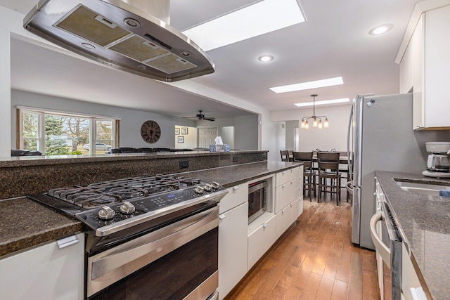 kitchen with white cabinets, dark stone counters, hardwood / wood-style flooring, appliances with stainless steel finishes, and ventilation hood