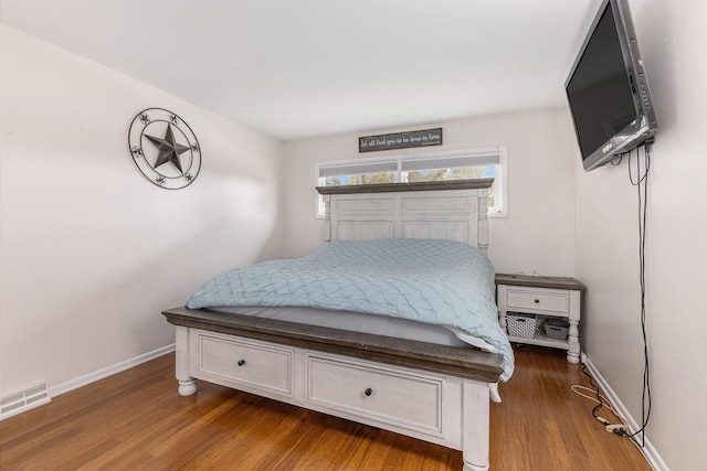 bedroom with baseboards, visible vents, and wood finished floors