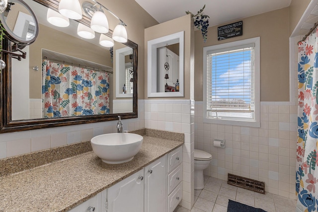 bathroom with tile walls, visible vents, toilet, vanity, and tile patterned flooring