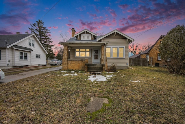 bungalow with a yard, brick siding, fence, and a chimney