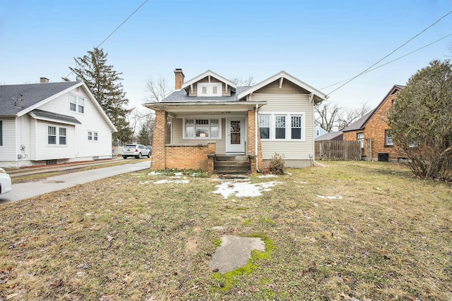 bungalow-style home featuring brick siding, a chimney, a front lawn, and fence