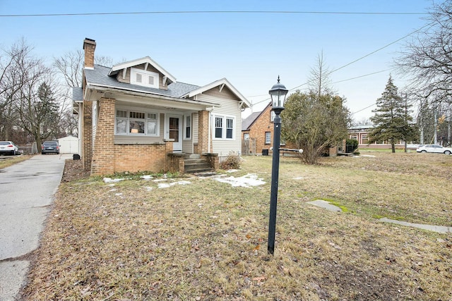 bungalow-style house featuring a garage, brick siding, a chimney, and a front yard