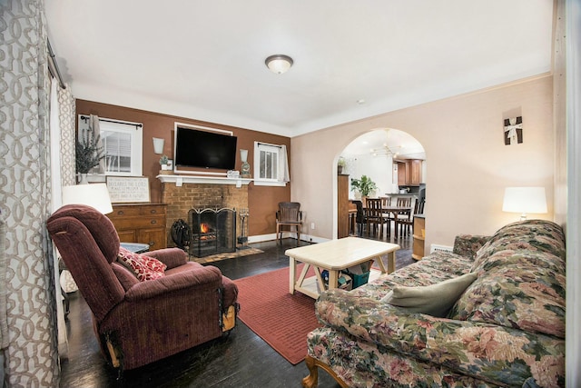 living area featuring a brick fireplace, baseboards, arched walkways, and wood finished floors