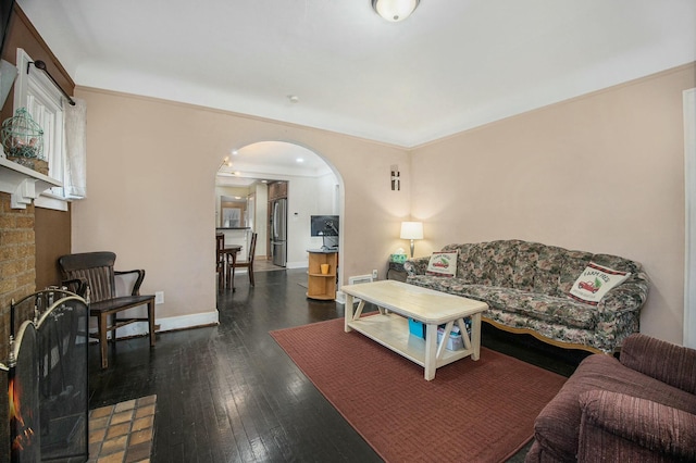 living room with baseboards, arched walkways, ornamental molding, dark wood-type flooring, and a brick fireplace