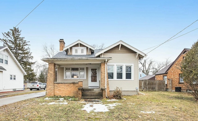 bungalow-style house featuring brick siding, a chimney, central AC unit, fence, and a front lawn