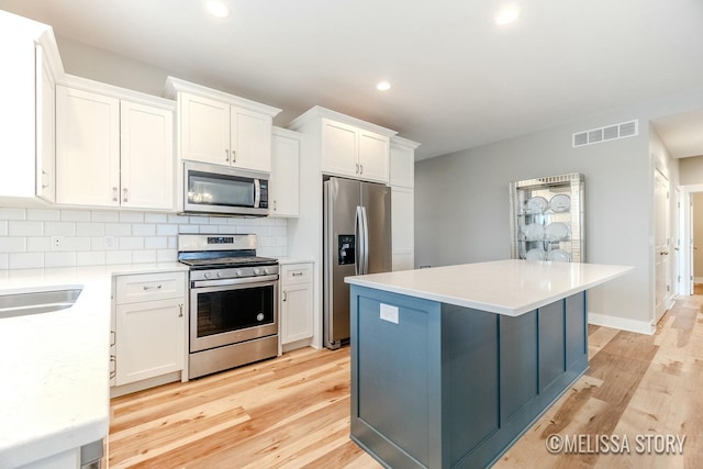 kitchen with stainless steel appliances, visible vents, backsplash, white cabinets, and light wood-type flooring