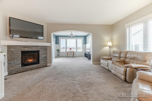 living area with arched walkways, a fireplace, a ceiling fan, baseboards, and carpet