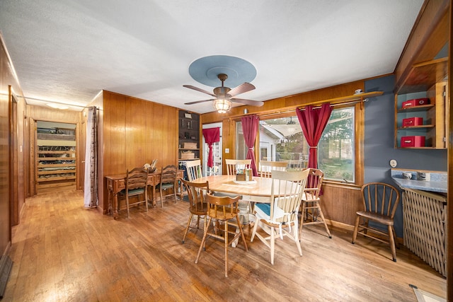 dining space with light wood-type flooring, ceiling fan, wooden walls, and radiator