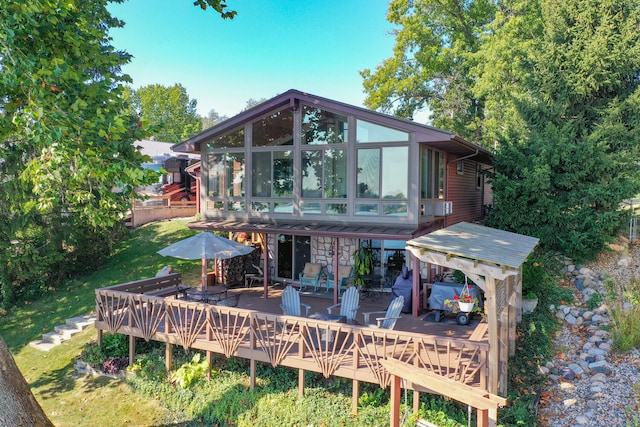 back of house featuring stone siding, outdoor dining area, a wooden deck, and a sunroom