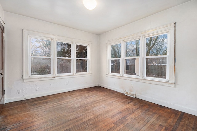 unfurnished room with baseboards, visible vents, and hardwood / wood-style floors