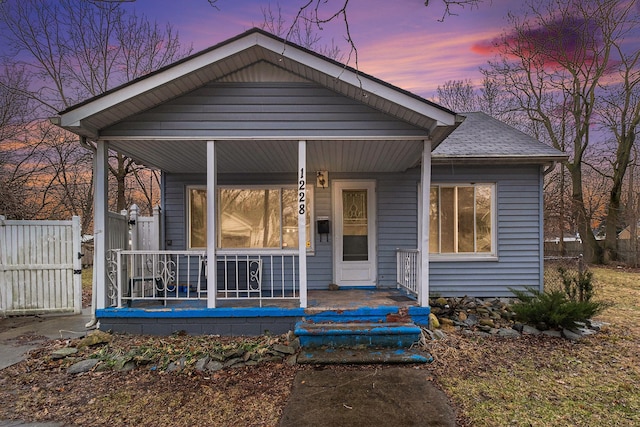 bungalow-style house with a shingled roof, fence, and a porch