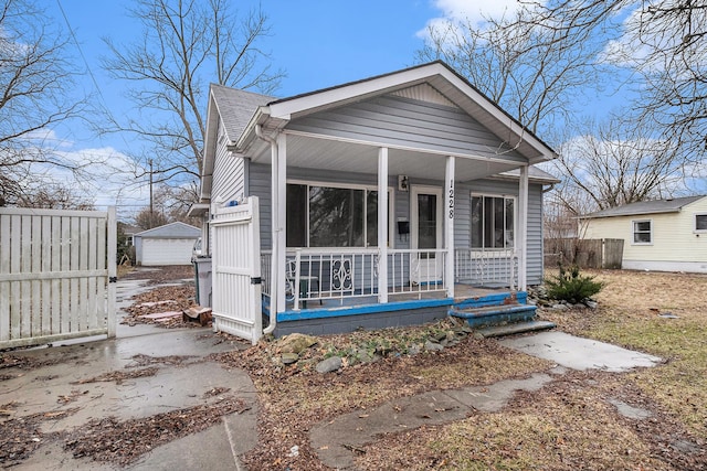 bungalow featuring a shingled roof, a detached garage, covered porch, fence, and an outdoor structure