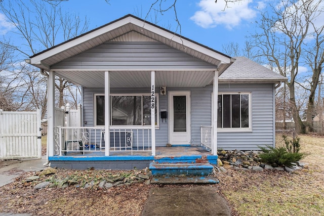 bungalow featuring a porch, roof with shingles, and fence