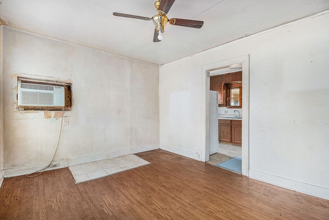 empty room featuring a sink, wood finished floors, a ceiling fan, baseboards, and a wall mounted air conditioner