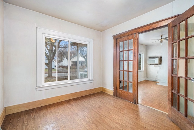 spare room with light wood-style floors, baseboards, an AC wall unit, and french doors