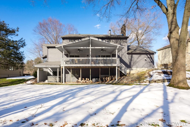 snow covered house featuring ceiling fan, a deck, stairway, and a chimney