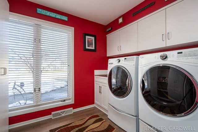 washroom featuring dark wood-style floors, washing machine and clothes dryer, visible vents, cabinet space, and baseboards