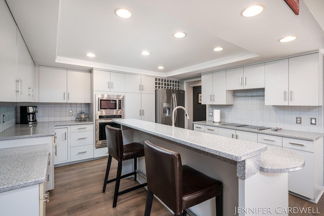 kitchen with dark wood-style floors, a kitchen island, a breakfast bar area, a tray ceiling, and stainless steel appliances