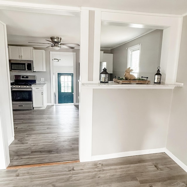 kitchen featuring ceiling fan, wood finished floors, baseboards, white cabinets, and appliances with stainless steel finishes