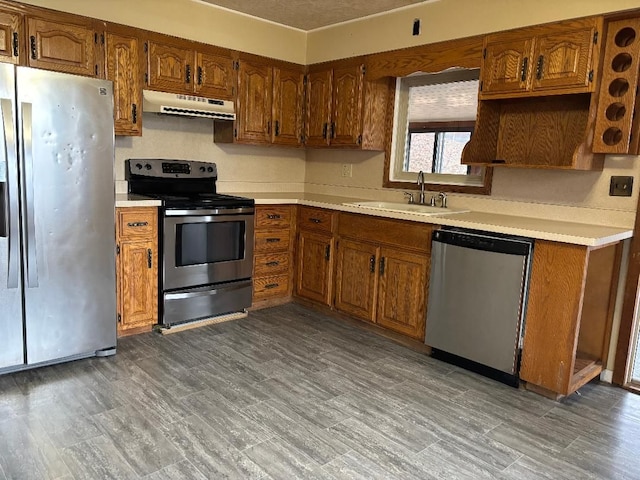 kitchen with appliances with stainless steel finishes, brown cabinets, light countertops, under cabinet range hood, and a sink