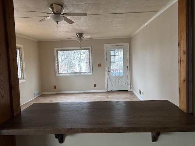 empty room with ornamental molding, visible vents, baseboards, and wood finished floors