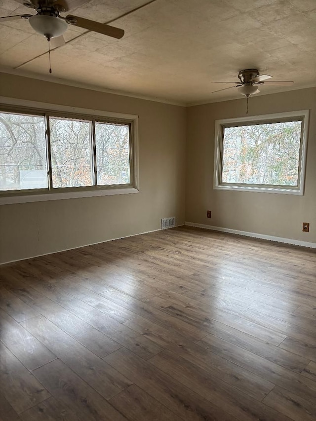 empty room featuring a ceiling fan, wood-type flooring, and a healthy amount of sunlight