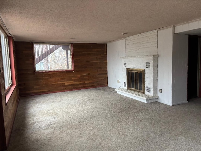 unfurnished living room with wooden walls, visible vents, a glass covered fireplace, a textured ceiling, and carpet floors