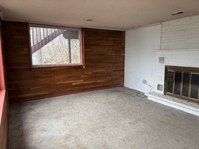 unfurnished living room featuring wooden walls, visible vents, a textured ceiling, carpet floors, and a fireplace