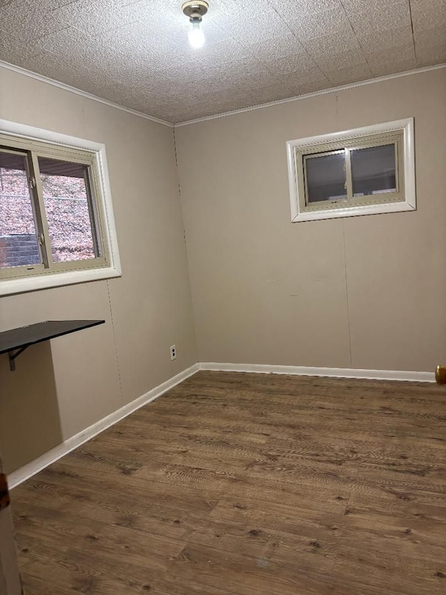 spare room featuring a textured ceiling, ornamental molding, dark wood-type flooring, and baseboards