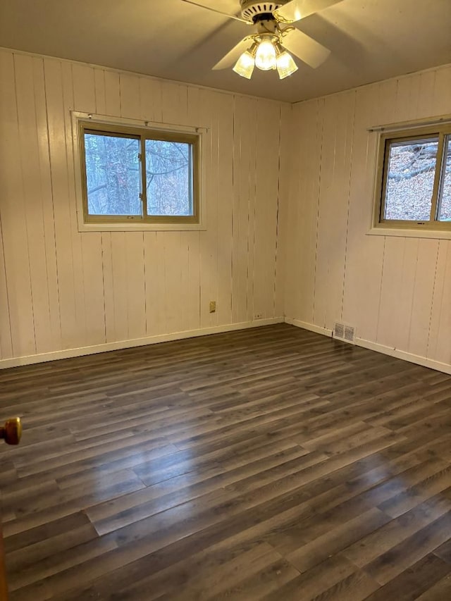 empty room featuring ceiling fan, dark wood-style flooring, visible vents, and baseboards