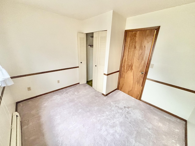 unfurnished bedroom with a baseboard heating unit, a closet, carpet flooring, and baseboards