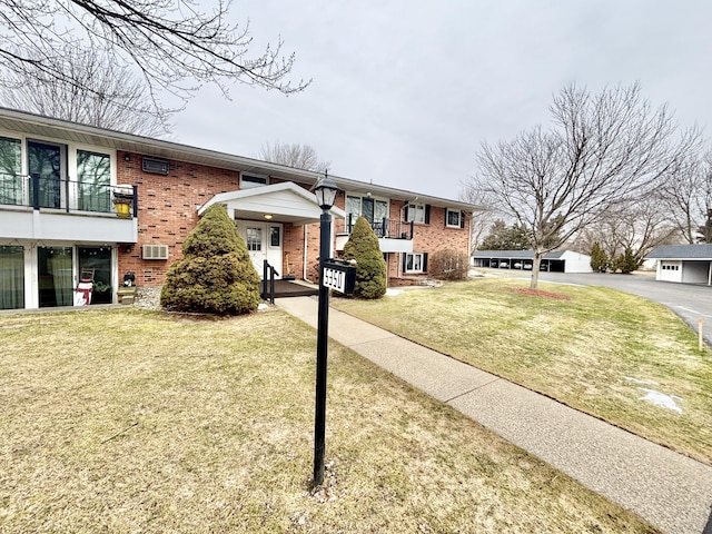 view of front of home featuring brick siding, a front lawn, a wall mounted AC, and a balcony