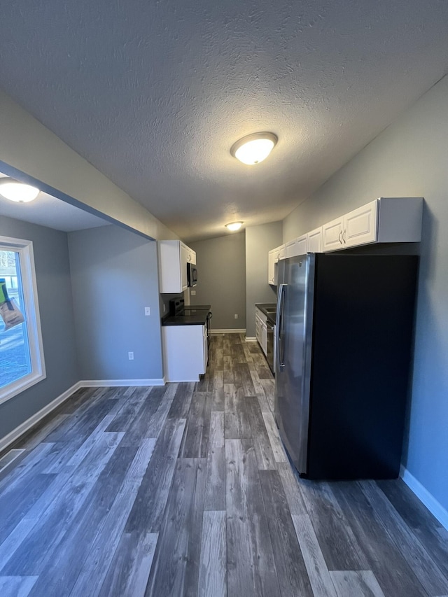 kitchen with dark wood-style flooring, white cabinetry, baseboards, appliances with stainless steel finishes, and dark countertops