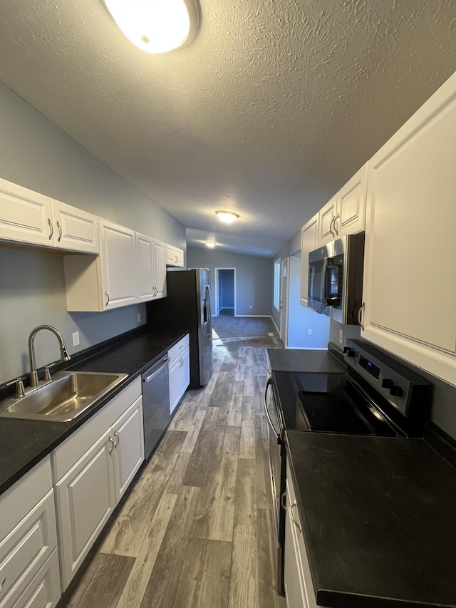 kitchen with stainless steel appliances, dark countertops, dark wood-type flooring, white cabinetry, and a sink