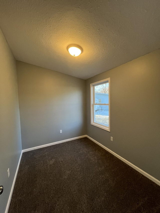 empty room with dark colored carpet, a textured ceiling, and baseboards