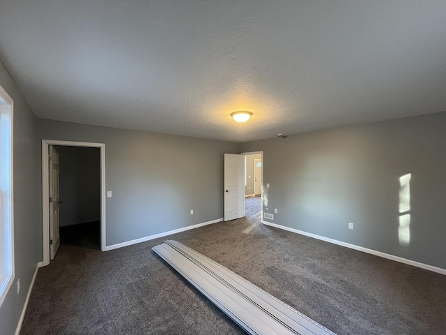 unfurnished room with dark carpet, a textured ceiling, and baseboards