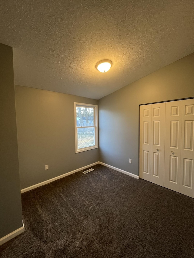 empty room featuring a textured ceiling, visible vents, baseboards, vaulted ceiling, and dark carpet