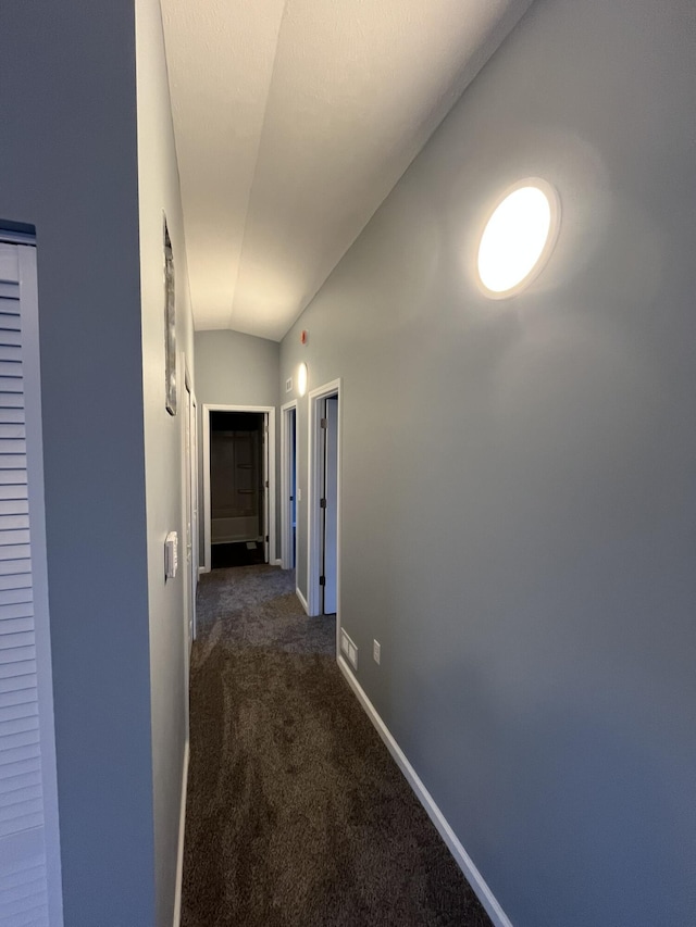 corridor featuring lofted ceiling, dark carpet, and baseboards