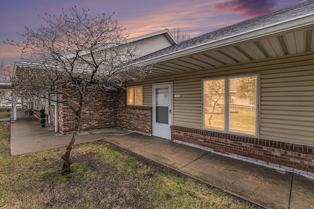 doorway to property with a shingled roof, brick siding, and a patio