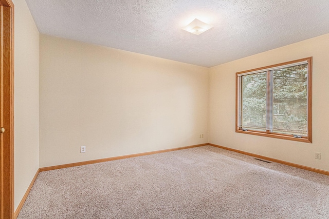 spare room featuring carpet floors, visible vents, a textured ceiling, and baseboards