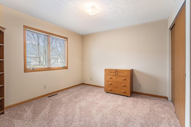 unfurnished bedroom with light carpet, a textured ceiling, a closet, and visible vents