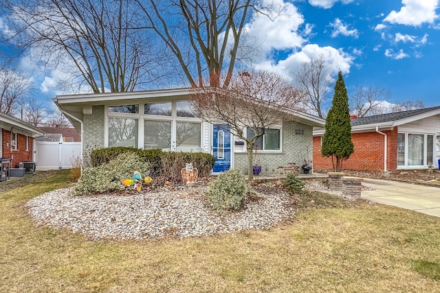 view of front facade featuring brick siding, fence, a front yard, central AC, and driveway