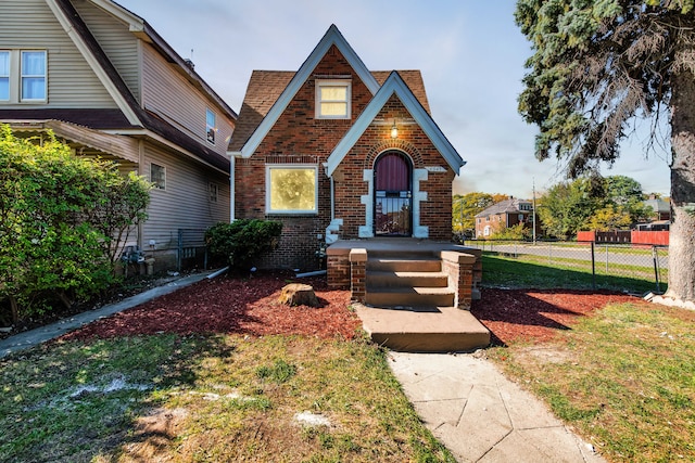 tudor-style house featuring a front yard, fence, and brick siding