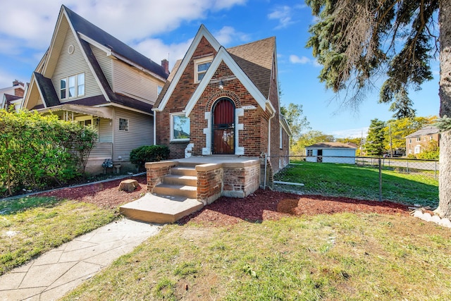 english style home with a front yard, fence, and brick siding