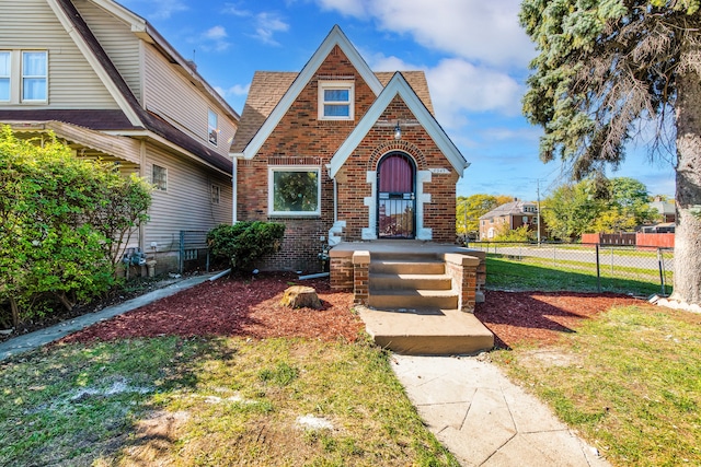 tudor house featuring brick siding, fence, and a front lawn