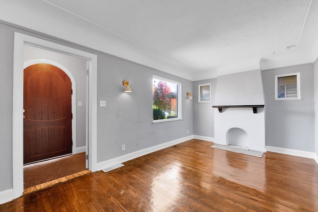 unfurnished living room featuring arched walkways, a fireplace, visible vents, baseboards, and hardwood / wood-style floors