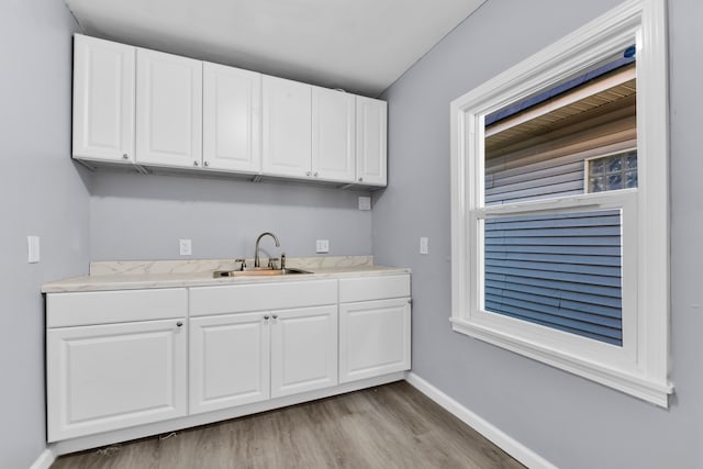 kitchen featuring wood finished floors, a sink, white cabinetry, baseboards, and light countertops